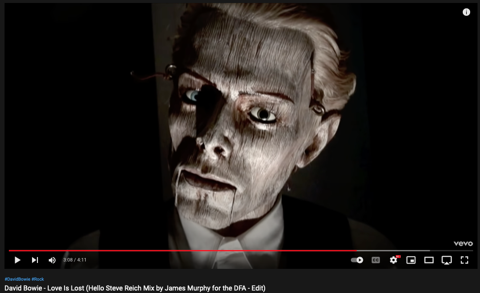 still from Bowie's "Love Is Lost" showing a wooden head likeness of David Bowie