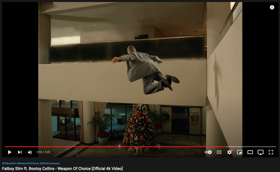Fatboy Slim - "Weapon of Choice" video still showing man flying over hotel lobby Christmas tree