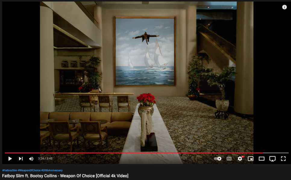 Fatboy Slim - "Weapon of Choice" video still showing man flying in front of painting of 3 sailboats on choppy water