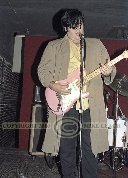 Chris playing at the Wrex wearing tan colored trenchcoat