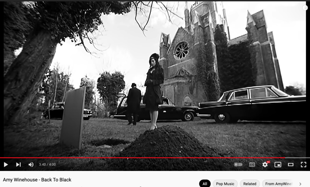 still from Amy Winehouse video Back To Black showing hill of dirt before open grave