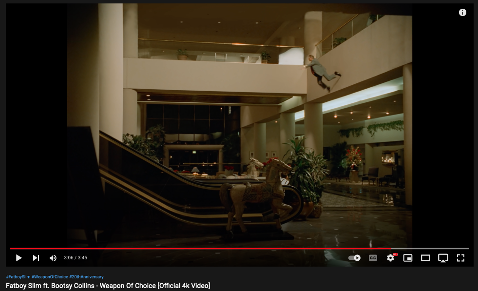 Fatboy Slim - "Weapon of Choice" video still showing man hovering in front of an escalator flanked by two large wooden horses